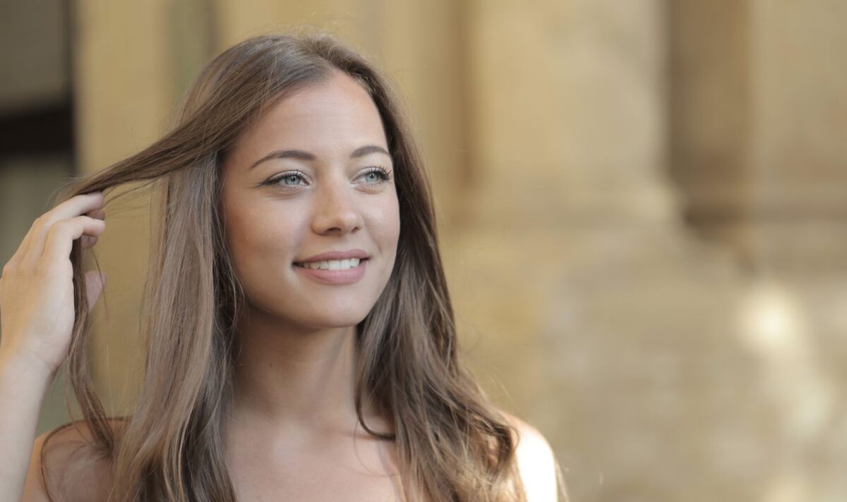 A young woman with long hair smiling while enjoying a sunny day outdoors.