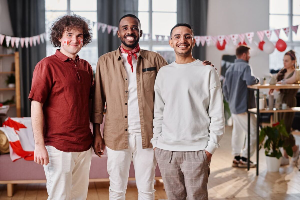 Three diverse men smiling and celebrating indoors with festive Canada Day decorations.